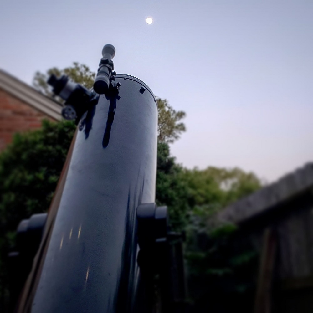 Telescope pointed towards the sky with the moon small and in the far distance.