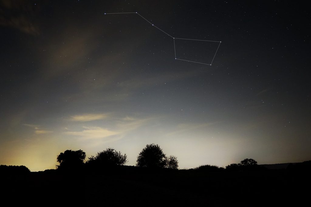 The night sky over a darkened landscape shows the outline of The Big Dipper constellation