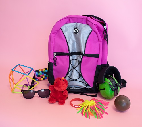 Pink backpack sits on a light pink background surrounded by various fidgets of different colors