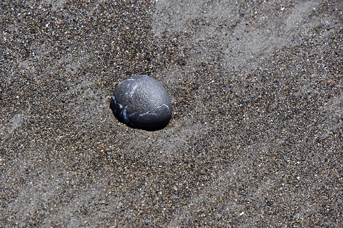 Dark gray egg shaped rock nestled in sand (not a dinosaur egg)